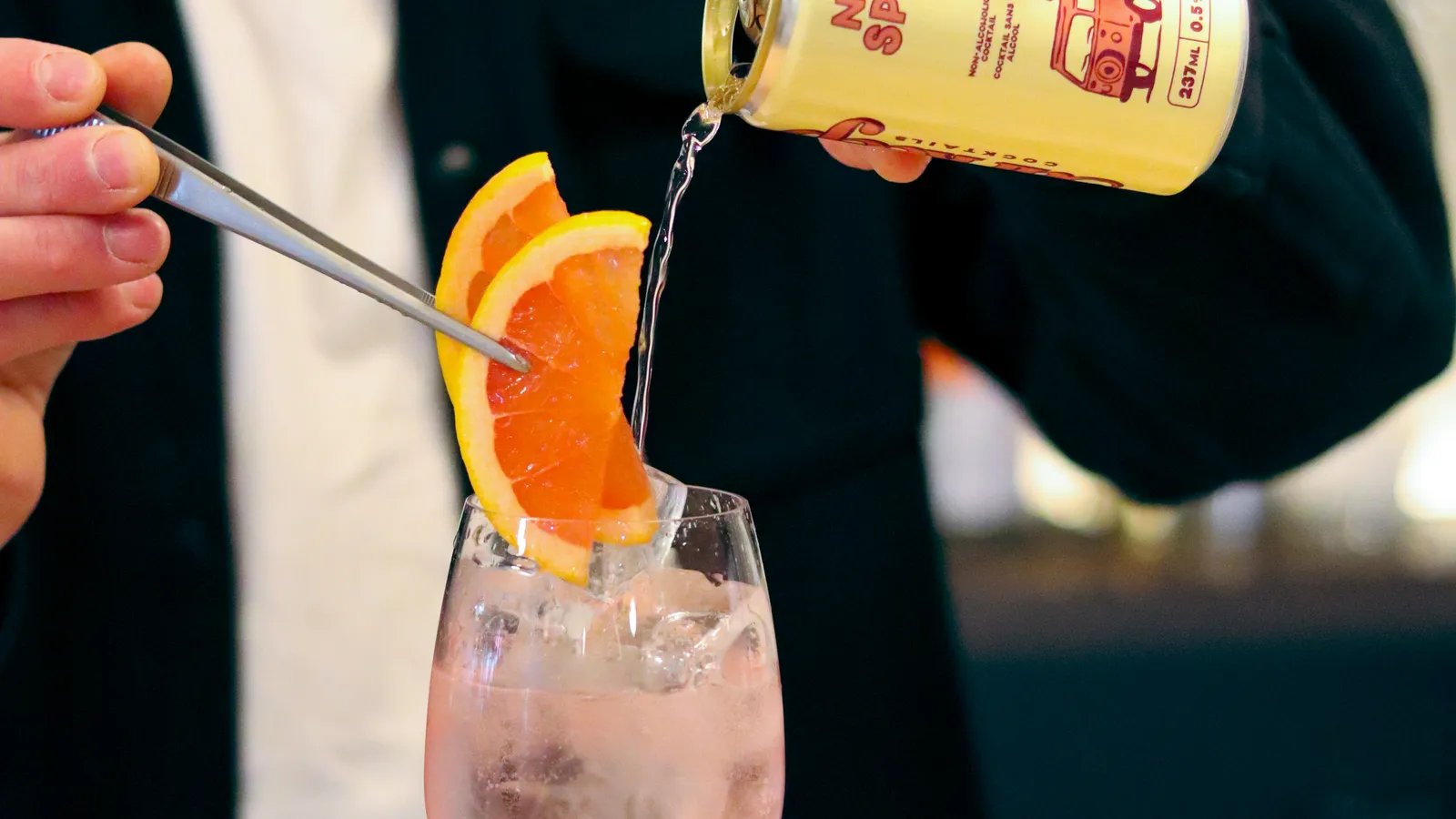 A bartender pours a can of Barkeep spritz over orange slices into a wine glass